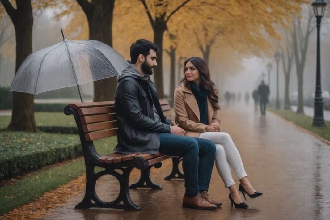 Two adults talking on a park bench beneath an umbrella on a rainy autumn day.