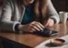 How to Stop Checking My Partner’s Social Media Constantly? What the Pattern Usually Means—and What to Do Next Close view of hands touching a phone screen on a cafe table beside a plain cup.