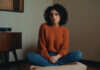 Why Being the “Cool Girl” Is Quietly Destroying Your Feminine Soul A woman in a rust sweater resting alone in a quiet room.