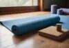 Yoga for Back Pain: Gentle Routines That Help A rolled yoga mat, plain cork blocks and a bolster beside a window.
