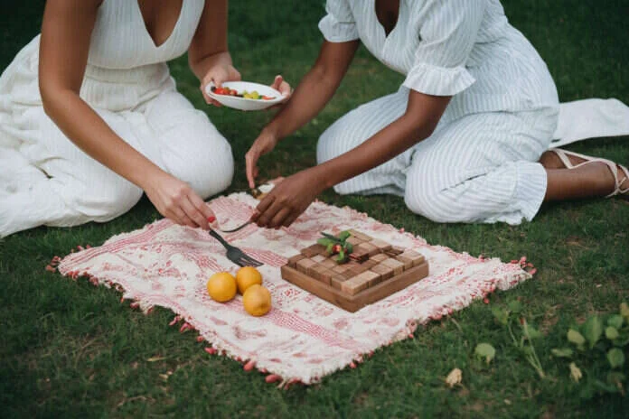 Two adults enjoying a picnic activity with food and a wooden game board.
