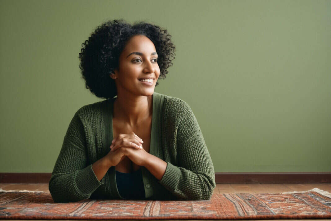 A woman sitting calmly with her hands clasped in a quiet room.